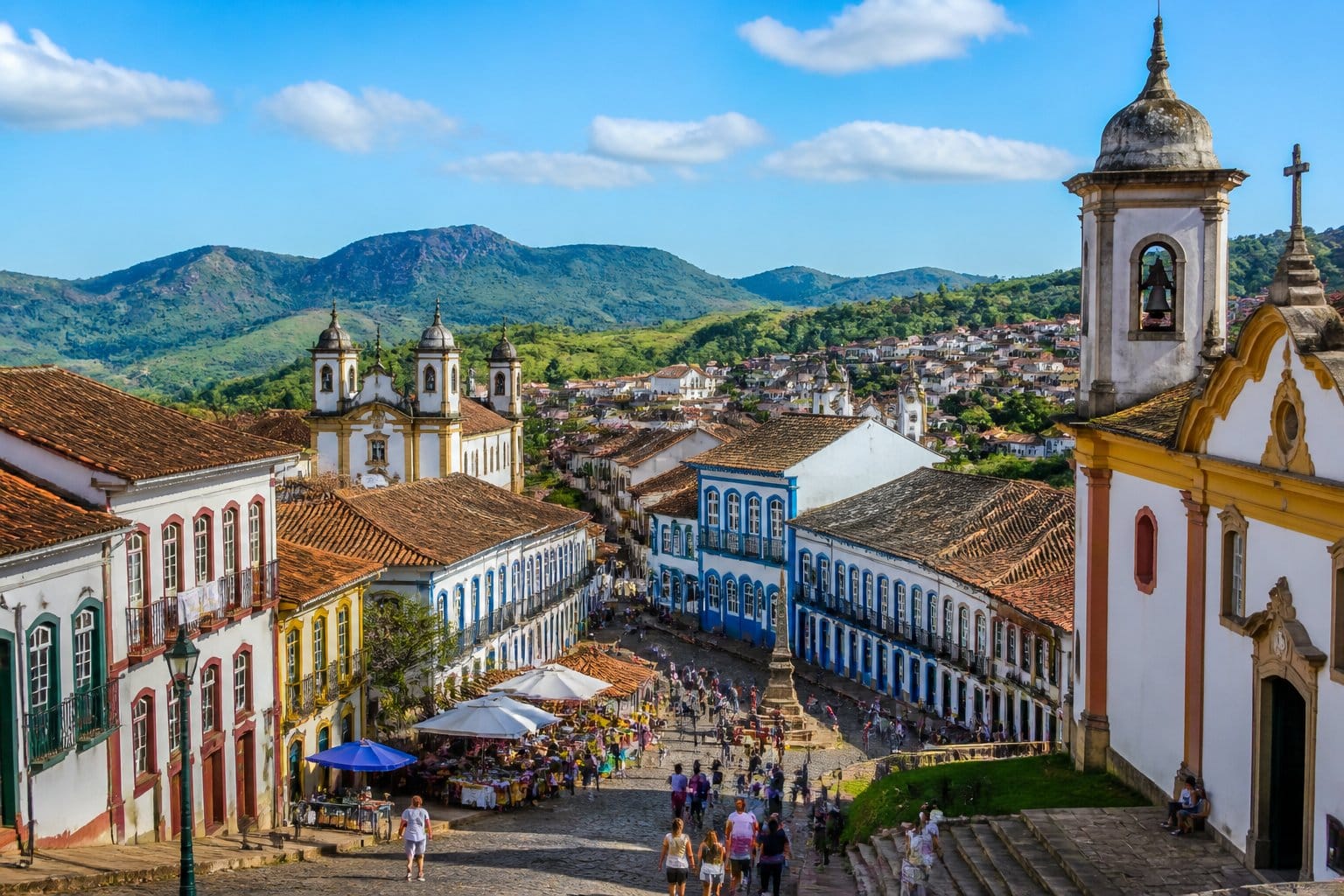 Vista panorâmica de uma cidade histórica próxima a Belo Horizonte com arquitetura colonial, ruas de paralelepípedos e pessoas nas praças.