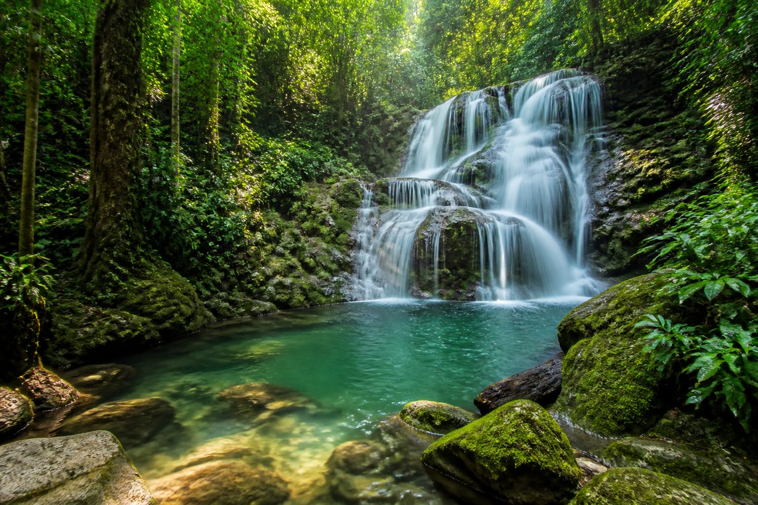 Cachoeira em uma floresta tropical com água caindo sobre pedras e vegetação verde ao redor.