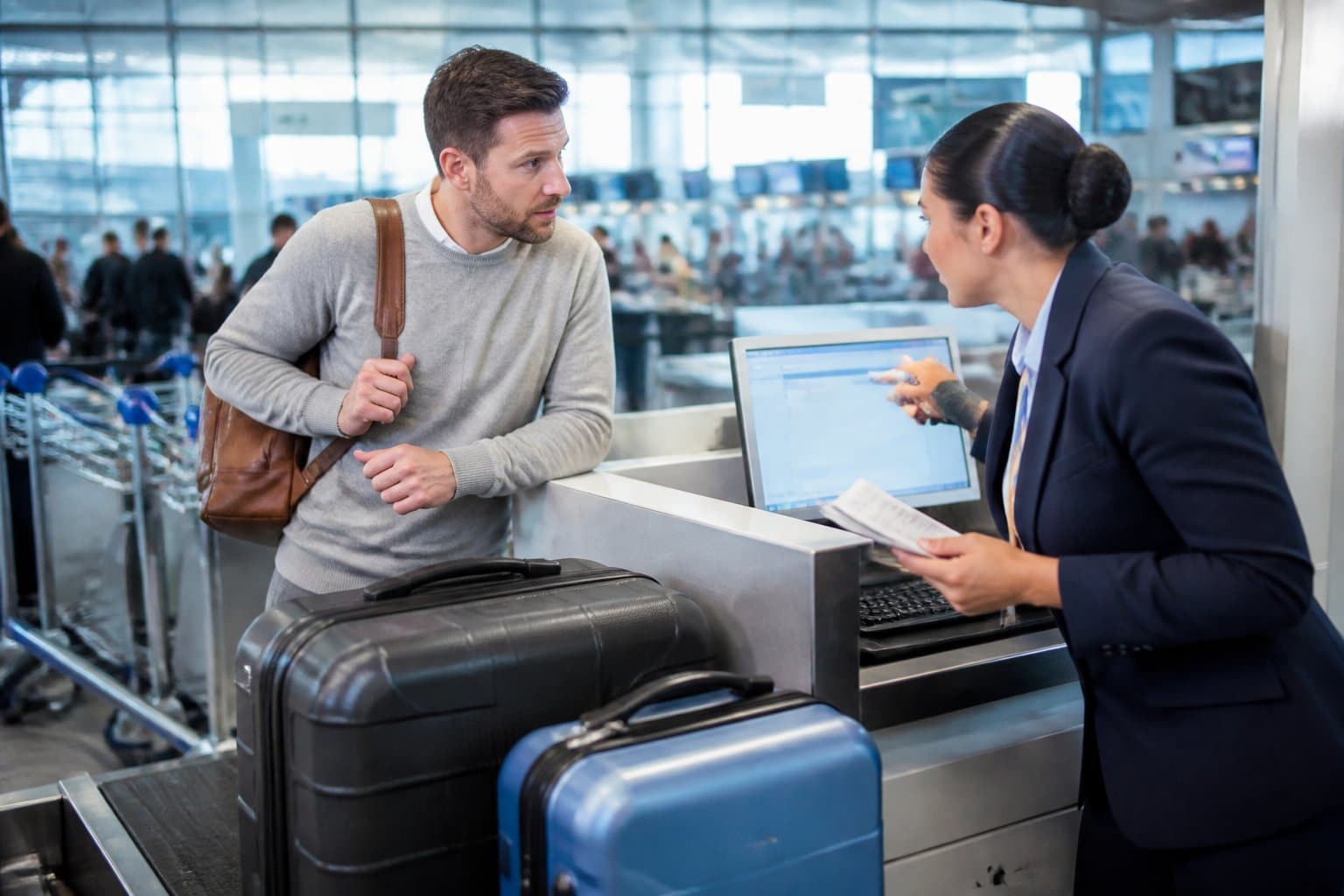 Passageiro conversando com funcionário da companhia aérea no balcão de check-in em um aeroporto, com malas sobre a balança.
